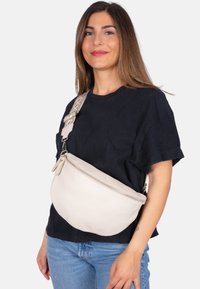 Weiße Lederbauchtasche mit einer geschwungenen Form, ausgestattet mit einem Reißverschluss, einem verstellbaren, gemusterten Gurt und einer strukturierten Oberfläche.