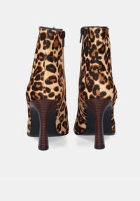 Un par de botas de tacón alto con estampado de leopardo, suela negra y tacones de aguja texturizados en marrón, mostradas desde la parte posterior sobre un fondo blanco.