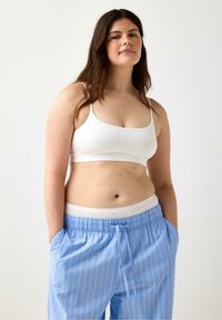 Valkoinen crop-top, jossa on ohuet olkaimet, yhdistettynä vaaleansinisempiin raidallisiin housuihin, joissa on joustava vyötärö ja nyöri, rento istuvuus.
