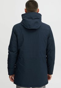 Marineblaue Winterjacke mit Kapuze, langen Ärmeln und geradem Schnitt. Das Material wirkt glatt und hat minimale sichtbare Beschläge.