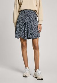 Gonna plissettata con stampa floreale in navy e fiori bianchi, tessuto leggero e vestibilità comoda. Indossata con una maglietta beige e sneakers chiare.