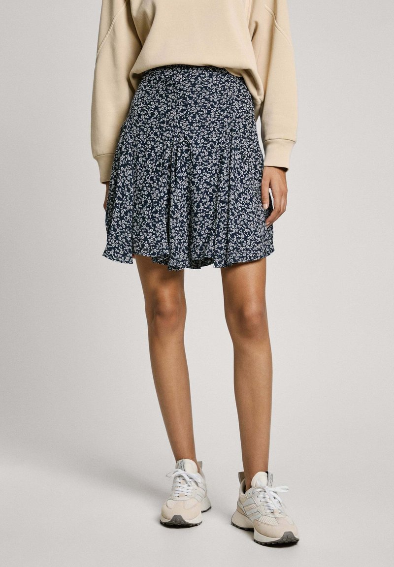 Gonna plissettata con stampa floreale in navy e fiori bianchi, tessuto leggero e vestibilità comoda. Indossata con una maglietta beige e sneakers chiare.