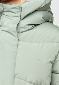 Minttu vihreä puhvijakku hupulla, jossa on sileä, kiiltävä pinta, ruudullinen rakenne ja hienovarainen "MAZINE"-logo painettuna kankaaseen.