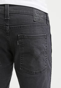 Mustat farkut, joissa on tekstuuripinta, viisi taskua, erottuva takataskusuunnittelu ja nahkainen brändilappu vyötäröllä.