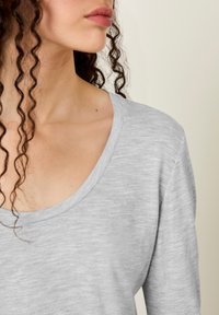 Gaiši pelēks, garām piedurknēm tops no mīksta, teksturēta auduma ar plašu apaļu izgriezumu un viegli vaļīgu piegriezumu.