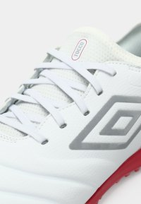 Bílé sportovní boty s šedými akcenty, texturovaným svrškem a červenou podrážkou. Vybavení zahrnuje kulaté tkaničky a logo "Tocco".