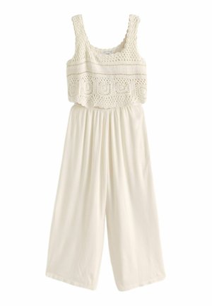 Combinaison blanche avec un corsage en crochet texturé à motifs carrés, un pantalon à jambe large et une coupe décontractée. Tissu doux, design sans manches.