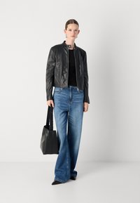 Črna usnjena jakna s okroglim ovratnikom, v kombinaciji s svetlomodrimi širokimi hlačami. Manekenka nosi črno torbo in ima na sebi črne špica čevlje.