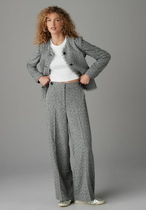 Szary garnitur z tkaniny w krate, w połączeniu z kurtką z krótkim frędzlem oraz spodniami o szerokich nogawkach, zestawiony z białą bluzką i srebrnymi sneakersami. Teksturowana tkanina, akcenty w postaci guzików.