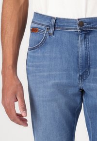 Τζιν σε ανοιχτό μπλε χρώμα. Σχέδιο με ψηλή μέση και κλασικό στυλ πέντε τσέπες, με μπρούντζινες λεπτομέρειες και διακριτές ραφές.