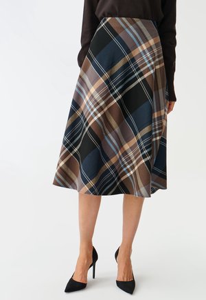 Woman wearing a knee-length A-line skirt with large navy, brown, beige, and light blue plaid pattern and black high-heeled shoes.