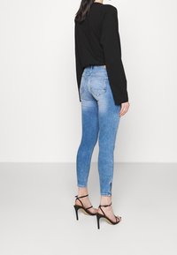 Ljusblå skinny jeans med en gradvis blekning, med två bakfickor. Kombineras med en svart långärmad topp och svarta sandaletter med remmar.