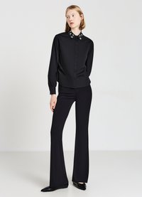 Schwarzes Hemd mit Knöpfen, besticktem Kragen, langen Ärmeln und taillierter Passform. Kombiniert mit schwarzen, ausgestellten Hosen und spitzen Ballerinas.