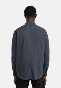 Chemise à manches longues gris foncé avec un col boutonné, couture arrière droite et poignets boutonnés. Fabriquée dans un tissu lisse avec une texture subtile.
