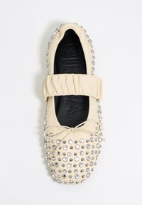 Ballerina in beige chiaro con strass tempestati, fascia elastica e materiale tessile morbido. Presenta punta rotonda e fiocco decorativo.