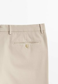 Beige broek met een gestructureerde stof, riemlussen en een achterzak met een knoopsluiting.