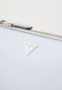 Portefeuille en matériau synthétique texturé bleu clair avec fermeture éclair dorée et détail de logo triangulaire de marque. Design compact avec une finition élégante.
