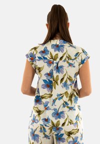 Blusa floral de tejido ligero con flores azules y naranjas sobre un fondo blanco. Las mangas cortas y un cuello completan el diseño.