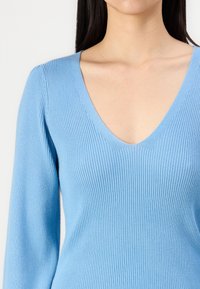 Pullover de malha canelada azul claro, com um decote em V profundo e mangas longas ajustadas, exibindo uma textura suave e uma silhueta justa.