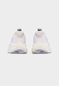 Ζευγάρι λευκών αθλητικών παπουτσιών Puma, εμφανιζόμενα από την πίσω πλευρά με υφή σόλας και μπεζ λεπτομέρειες, σε απλό λευκό φόντο.