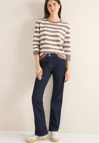 Maglione a righe marrone e bianco in maglia, con scollo rotondo, abbinato a jeans blu scuro con cuciture a contrasto e scarpe da ginnastica.