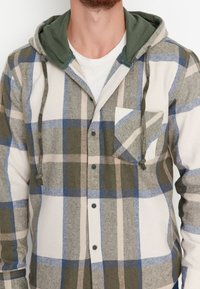 Camicia flanella a quadri con cappuccio verde, con colori blu, grigio e beige. Include una tasca sul petto e chiusura con bottoni frontali.