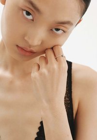 Anillo de plata con una gema azul, con una bandita delicada y pequeñas piedras claras. La mano del modelo toca suavemente su rostro, con una textura de piel suave.