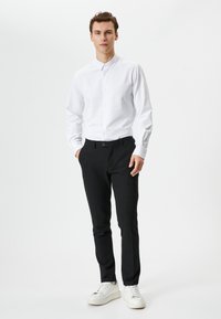 Camisa blanca de manga larga con un patrón sutil, combinada con pantalones negros ajustados y zapatillas blancas. Diseño entallado, textura suave.