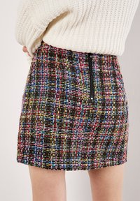 Mini gonna in tweed multicolore con un motivo testurizzato. Presenta una cerniera nera sul retro e un design aderente.