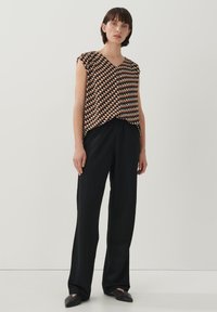 Bruine en witte patroonloze mouwloze top met een V-hals, gecombineerd met zwarte wijde broek en zwarte instap schoenen. Eenvoudig en modern ontwerp.