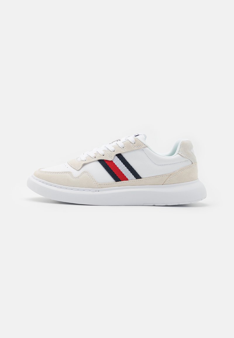 Sneaker bianca con dettagli in suede beige, caratterizzata da strisce nere e rosse. Suola bianca spessa, punta rotonda e design con lacci.
