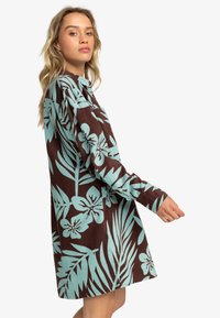 Long-sleeve dress with a brown base, featuring a teal botanical print of flowers and leaves. Relaxed fit with a button-up collar.