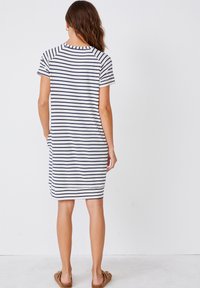 Pasiasta sukienka z krótkim rękawem w kolorach białym i granatowym. Charakteryzuje się luźnym fasonem, okrągłym dekoltem oraz bocznymi kieszeniami. Wykonana z gładkiej bawełnianej dzianiny jersey.