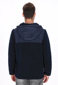 Chaqueta de forro polar azul marino con superficie texturizada y capucha de nailon lisa. Cuenta con mangas largas y un ajuste casual, ideal para usar en capas.