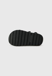 Sole di sandalo nera caratterizzata da un materiale gommoso texturizzato con scanalature orizzontali e verticali per una migliore aderenza, e un piccolo etichetta del marchio incorporata.
