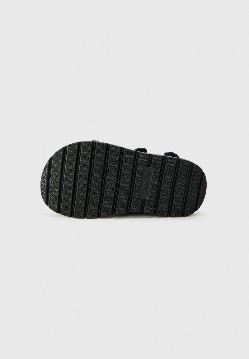 Schwarze Sandalensohle aus einem strukturierten Gummimaterial mit horizontalen und vertikalen Rillen für besseren Halt sowie einem kleinen, eingearbeiteten Markenlabel.