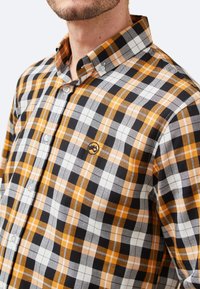 Camisa de cuadros en negro, blanco y naranja. Confeccionada en tela, con cuello, botones y logo bordado. Presenta un corte regular y un patrón.