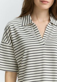 Polo a righe con scollo a V profondo, realizzato in tessuto morbido. Presenta righe alternanti blu navy e crema, con maniche corte e una vestibilità rilassata.