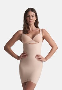 Abito modellante beige con un design aderente. Presenta una scollatura profonda e spalline sottili. Tessuto liscio e elasticizzato.
