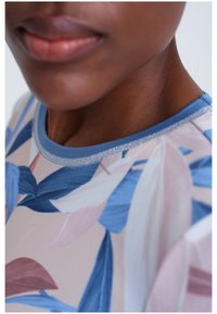 Vêtement à motif floral avec des feuilles bleues, roses et blanches. Encolure ronde avec un liseré bleu clair et des accents métalliques subtils.