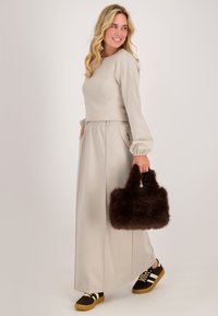 Licht beige lange mouw jurk met een getailleerde taille, gecombineerd met een bruine fluffy handtas en donkerbruine sneakers met witte strepen.