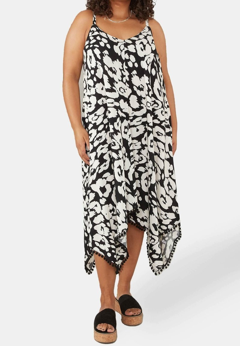 Svart och vit blommönstrad klänning med en flödande, asymmetrisk nederkant, tunna axelband och pom-pom detaljer i botten. Bärs med svarta sandaler.