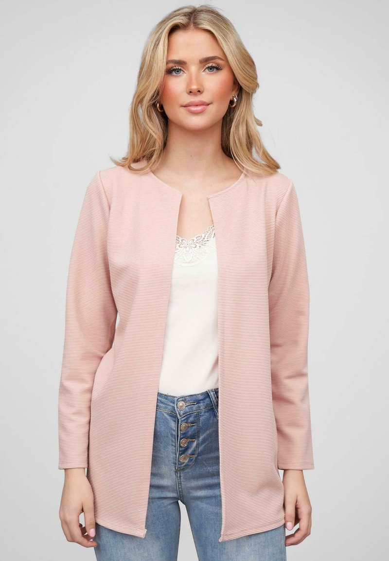 Lichtroze lange mouwen cardigan in een textuurstof met een open voorkant ontwerp. Gedragen over een witte kant tanktop en gecombineerd met blauwe jeans.