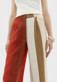 Pantaloni a righe con colori alternati di rosso, marrone e crema. Realizzati in tessuto leggero con una vestibilità rilassata e tasche laterali.