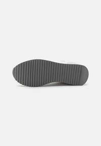 Shoe sole with a thick, gray rubber material featuring horizontal grooves for traction and a rounded back edge.