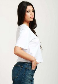 Maglietta bianca corta con maniche corte, abbinata a jeans a vita alta di colore blu scuro con tasca posteriore e dettagli di cucitura in vista.