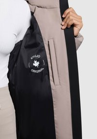 Schwarz-beige Jackeninnenseite mit einem Logo in Form eines Ahornblatts, gefüttertem Stoff, einer Seitentasche und glatter Textur.