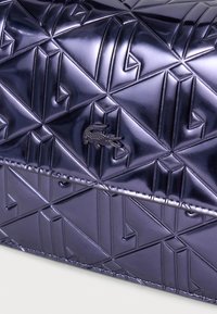 Borsa viola con fantasia geometrica realizzata in materiale lucido, caratterizzata da una superficie testurizzata e un piccolo logo ricamato in nero.