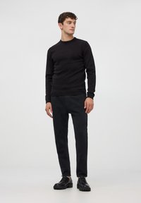 Maglione nero lavorato a maglia con colletto rotondo, abbinato a pantaloni neri slim-fit e scarpe nere con lacci, presentato su uno sfondo neutro.