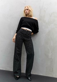 Črn off-shoulder pulover v kombinaciji z visokim pasom črnih hlačami z leopardjim vzorcem in koničastimi petami. Mehka tkanina, sproščen kroj, podroben vzorec.